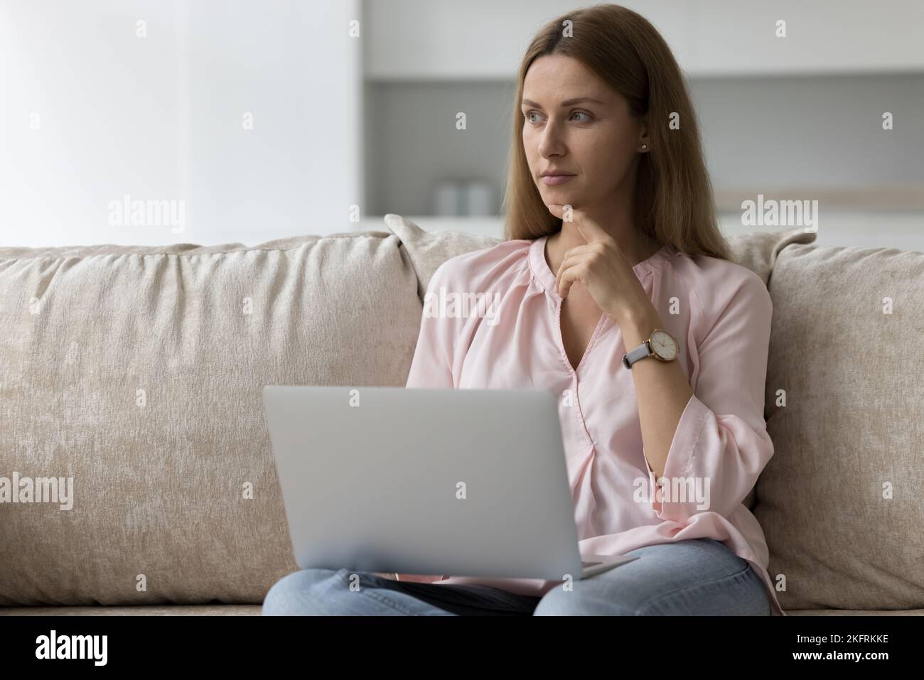 Una mujer reflexione sobre responder a un cliente que trabaja en casa utilizando un ordenador portátil Foto de stock