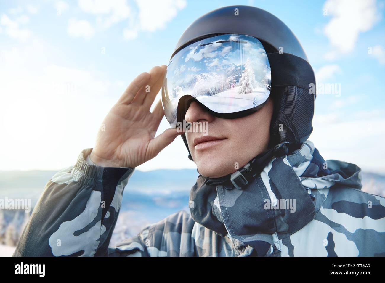 Retrato del hombre en el cielo azul de fondo sostiene gafas de esquí con el reflejo de las montañas nevadas..Deportes de invierno. Foto de stock