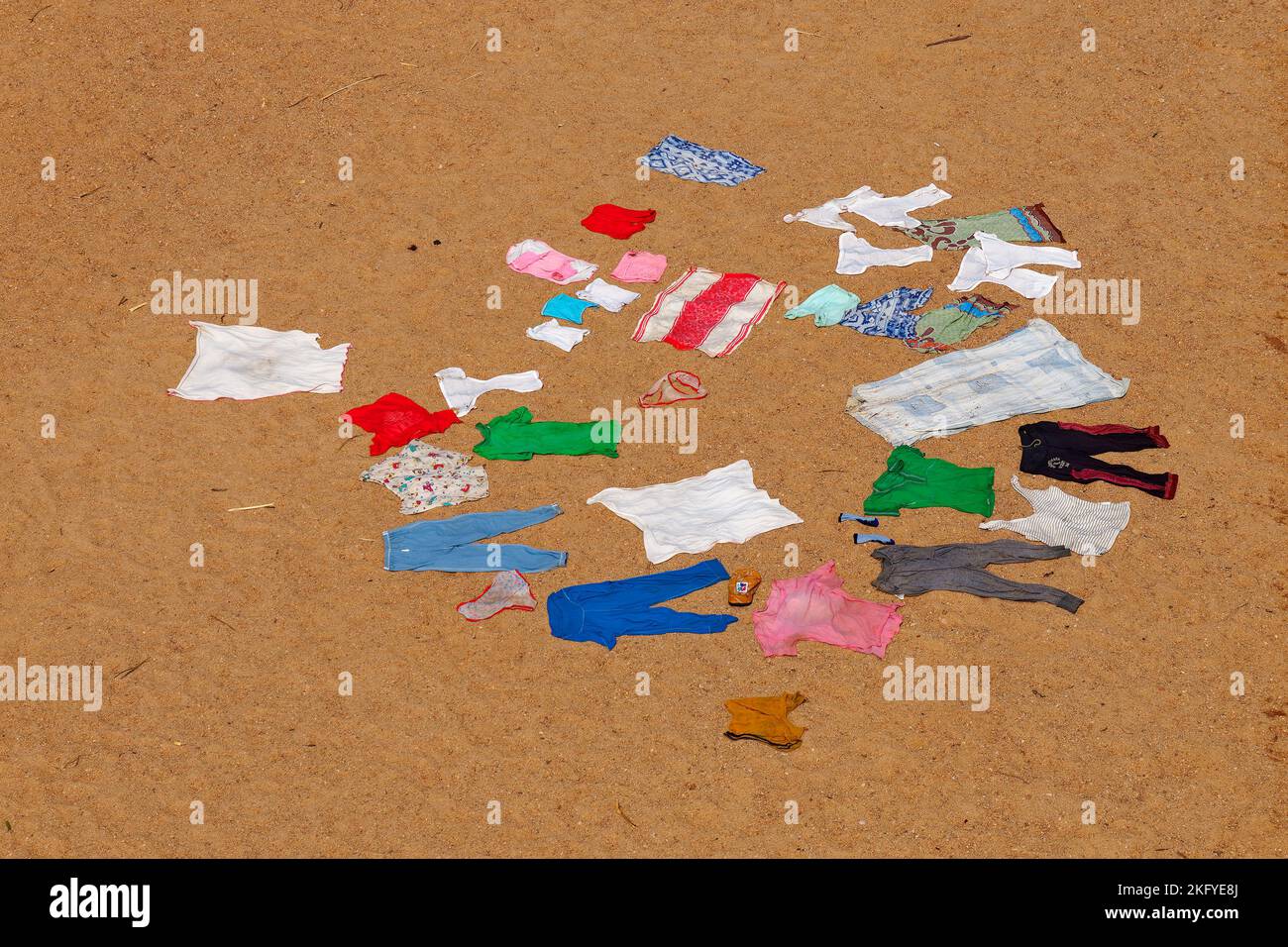 Secado de la ropa de colores lavados en el suelo arenoso y caliente sol africano, escena típica de la campiña africana. PIN rojo, azul, blanco y verde Foto de stock