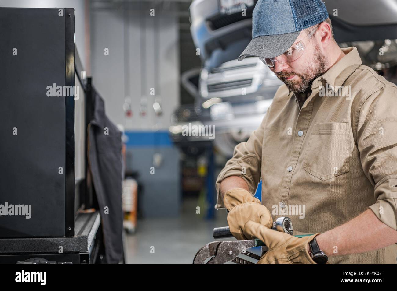 Mecánico caucásico profesional con herramienta en sus manos Preparándose para la reparación del vehículo. Taller de Automóviles en el Fondo. Foto de stock