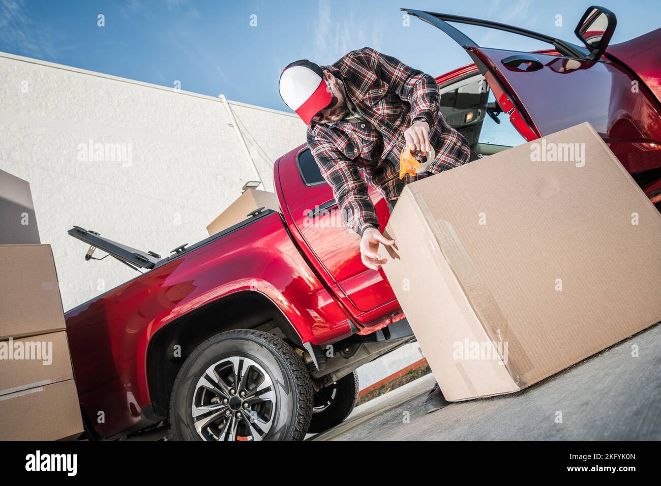 Profesional Mover sellando una caja de cartón usando cinta de embalaje para asegurar un transporte seguro. Tema de servicios de reubicación. Foto de stock