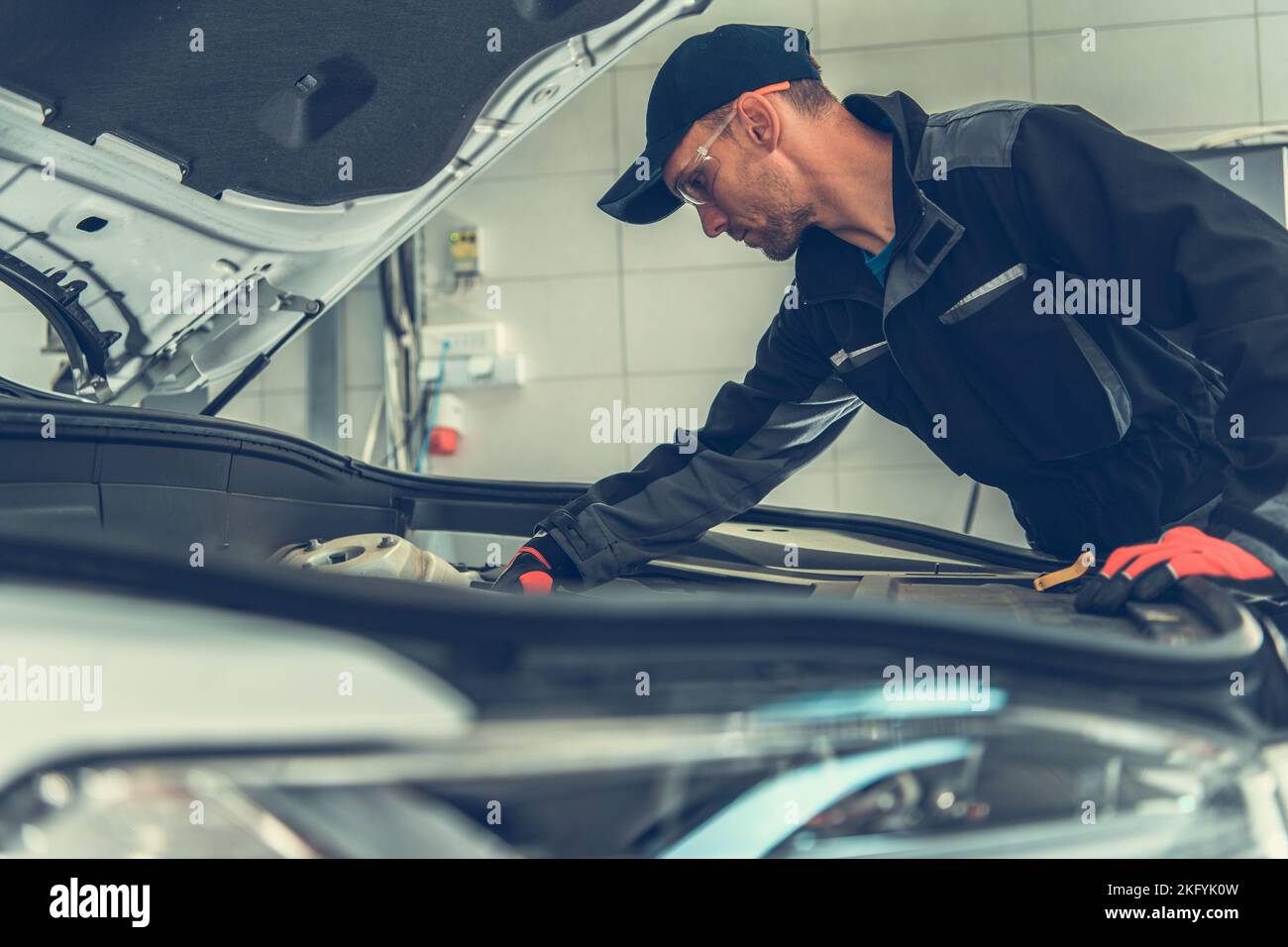 Mecánico caucásico profesional buscando debajo del capó del vehículo en su taller. Tema de servicios de reparación de automóviles. Foto de stock