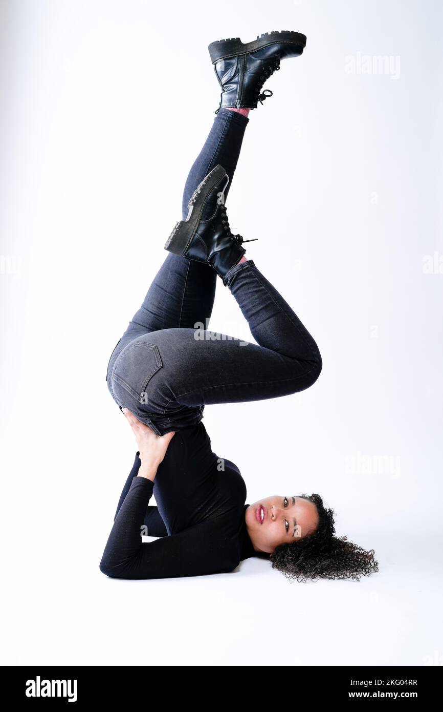 Joven mujer multirracial haciendo soporte de hombro pateando las piernas en el aire | Ropa de calle | Fondo blanco con espacio de copia Foto de stock