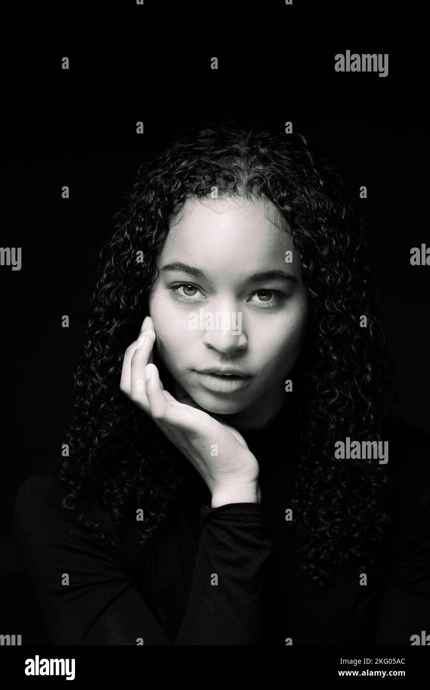Blanco y negro Primer plano Retrato de una joven mujer multirracial con las manos Framing de cara | Conjunto negro sobre fondo negro Foto de stock