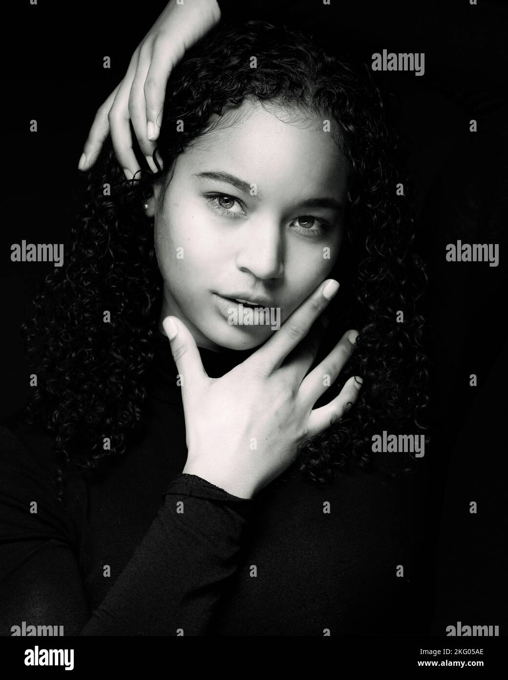 Blanco y negro Primer plano Retrato de una joven mujer multirracial con las manos Framing de cara | Conjunto negro sobre fondo negro Foto de stock