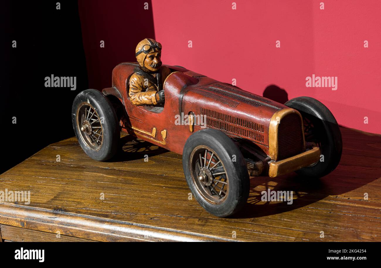 Modelo de madera retro de un coche de carreras colocado en un estante iluminado por el sol contra la pared roja en casa Foto de stock