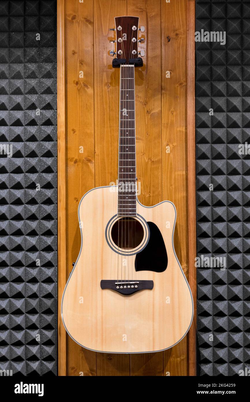 Guitarra clásica de madera con figura negra en la tabla de sonido colocada en la pared del moderno estudio de grabación Foto de stock