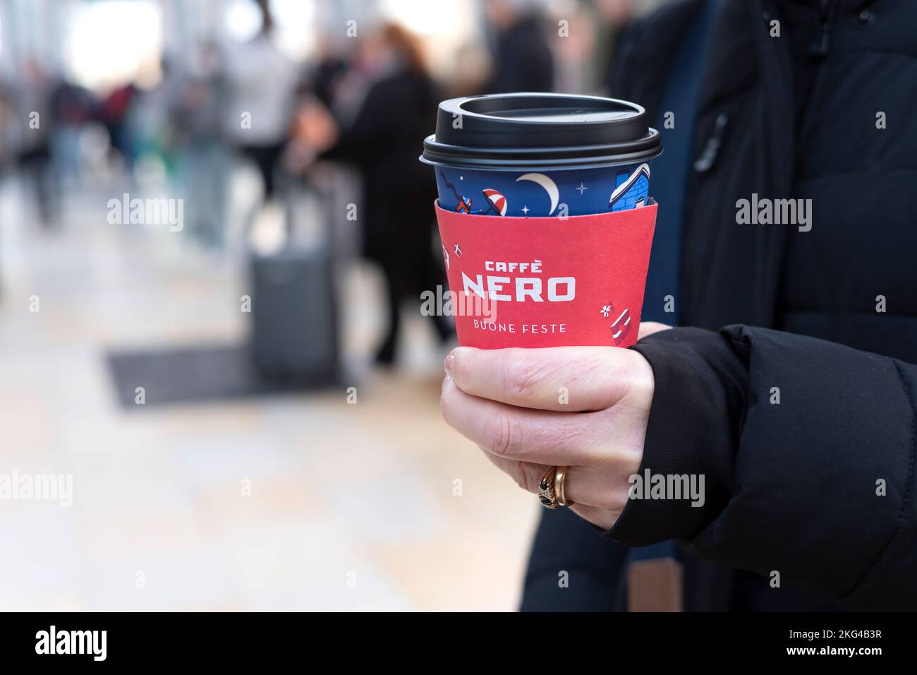 Una mujer sosteniendo una taza festiva de café para llevar de nero caffe. La taza de cartón tiene un mensaje festivo en italiano y muestra el logotipo de la marca Cafe Nero Foto de stock