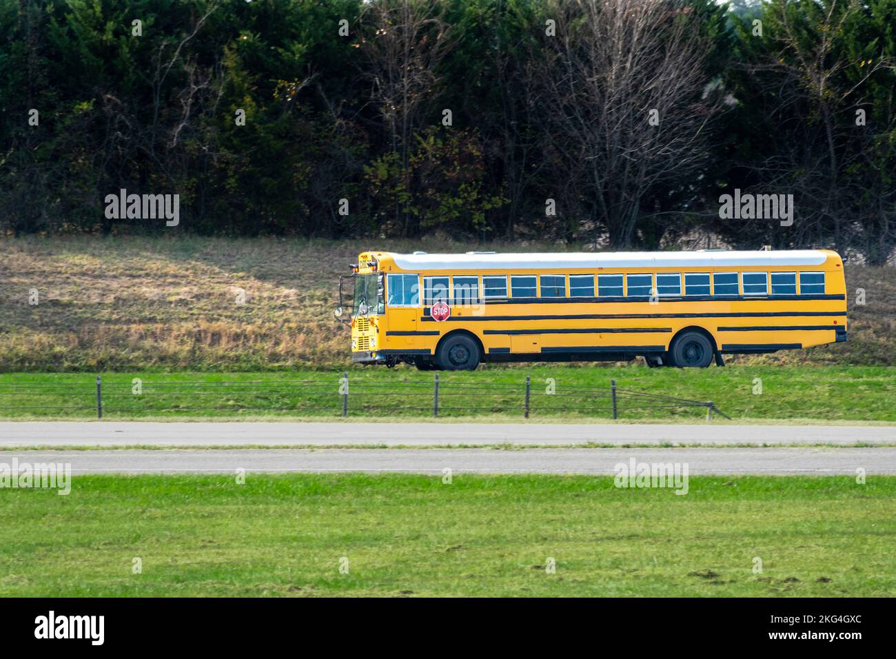 Plano horizontal de un largo autobús escolar en una carretera vacía. Las ondas de calor crean un ligero efecto ondulado Foto de stock