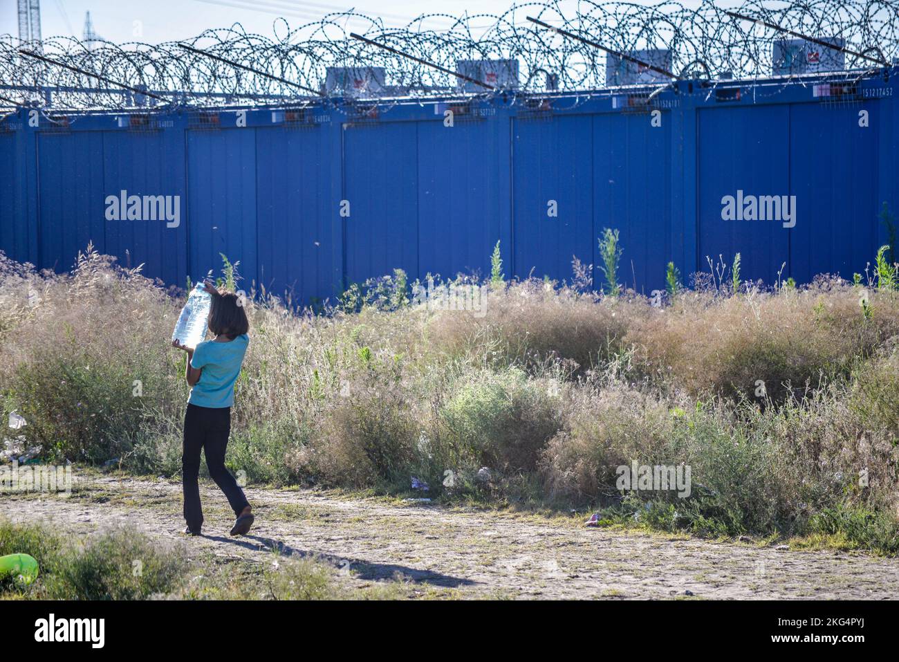 Niña que lleva agua potable. Desafiando las condiciones de vida en el campo de tránsito improvisado de migrantes/refugiados en la frontera entre Serbia y Hungría. Foto de stock