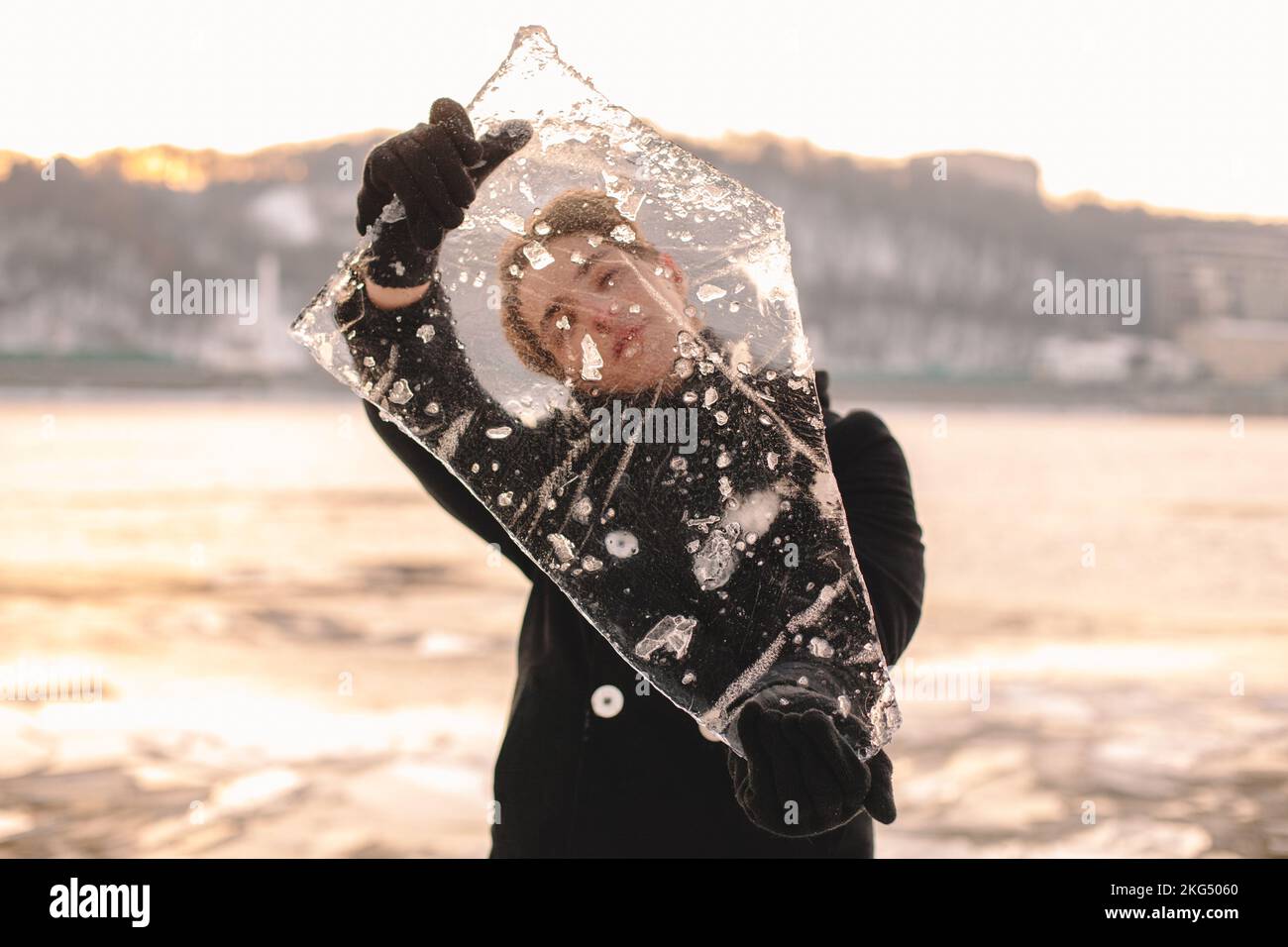 Adolescente mirando a través de un pedazo de hielo mientras lo sostiene de pie al aire libre durante el frío clima frío en invierno Foto de stock
