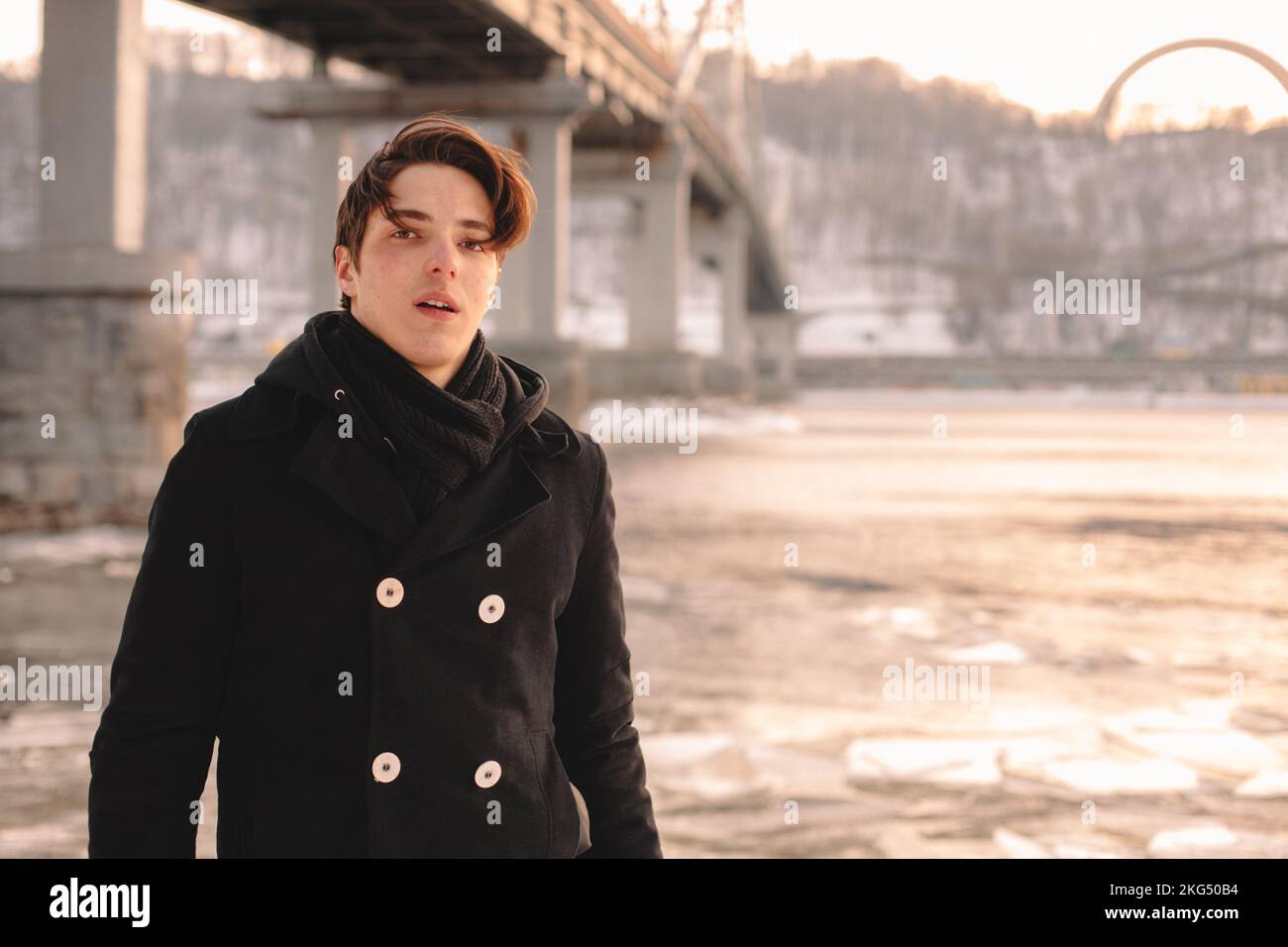 Retrato de un adolescente que llevaba abrigo y bufanda mientras estaba de pie junto al río en invierno Foto de stock