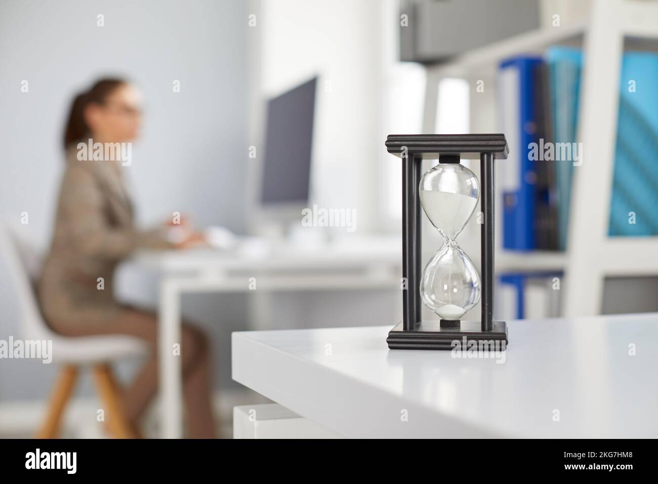 Sandglass en el escritorio de la oficina difuminar el fondo con una mujer trabajando en el ordenador. Foto de stock