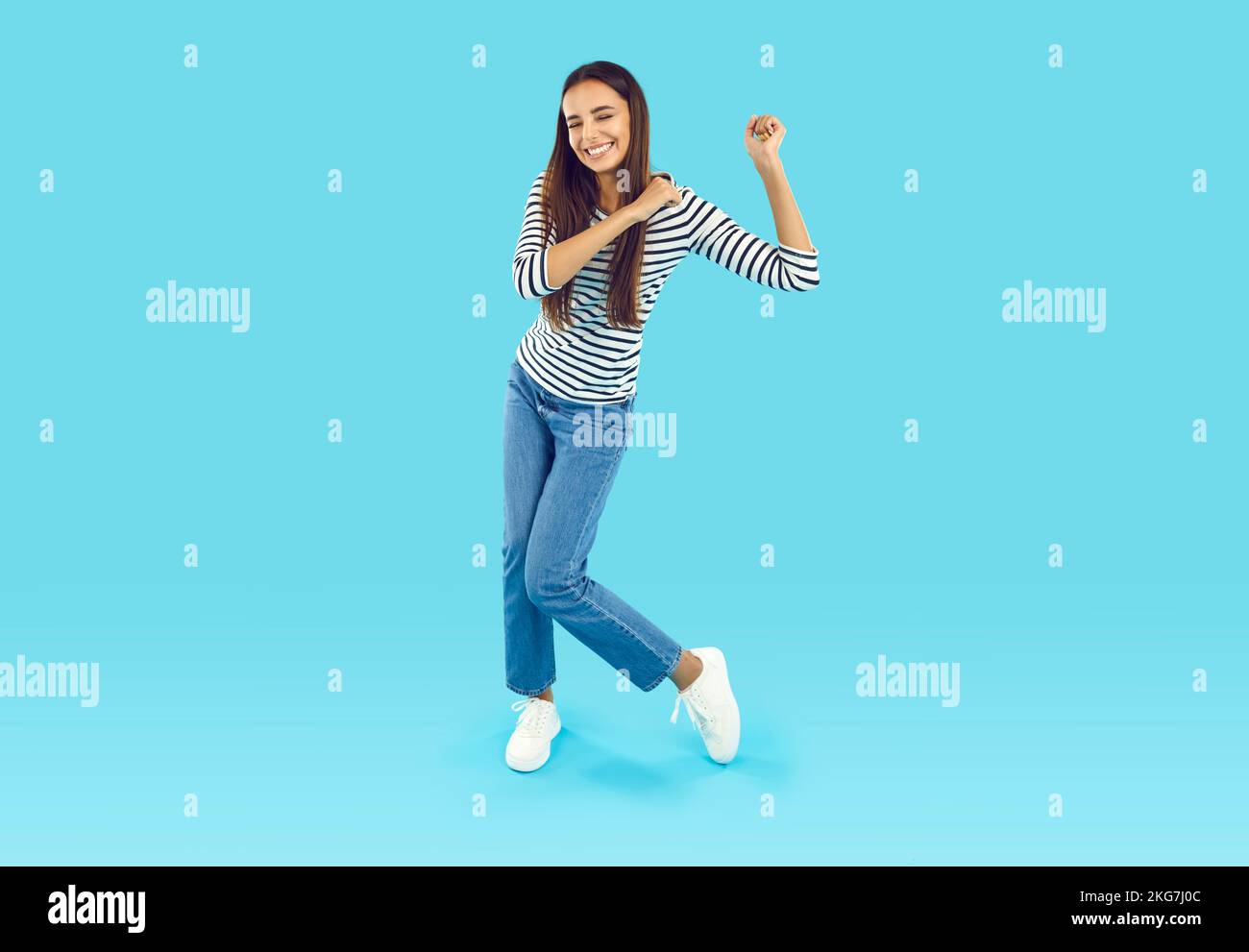 Foto a tamaño completo de una joven morena en una sudadera a rayas y jeans azules que se engañan y bailan Foto de stock