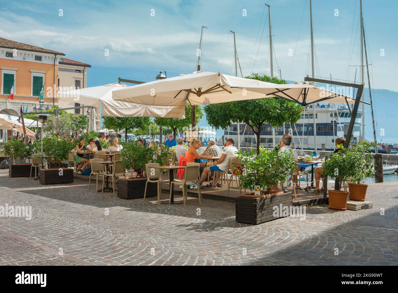 Italia lago de verano, vista de la gente que se relaja en un café al lado del lago terraza en Piazza Feltrinelli en el pintoresco Lago Garda ciudad de Gargnano, Lombardía, Italia Foto de stock