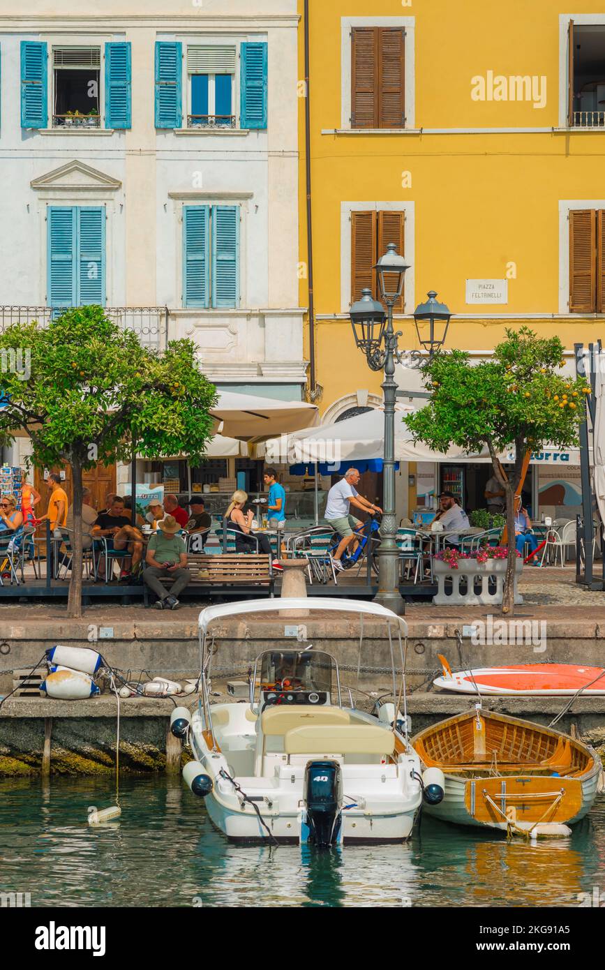 Italia café, vista en verano de la gente que se relaja en las terrazas de café frente al mar en la pintoresca ciudad a orillas del lago de Gargnano, Lago de Garda, Lombardía, Italia, Europa Foto de stock