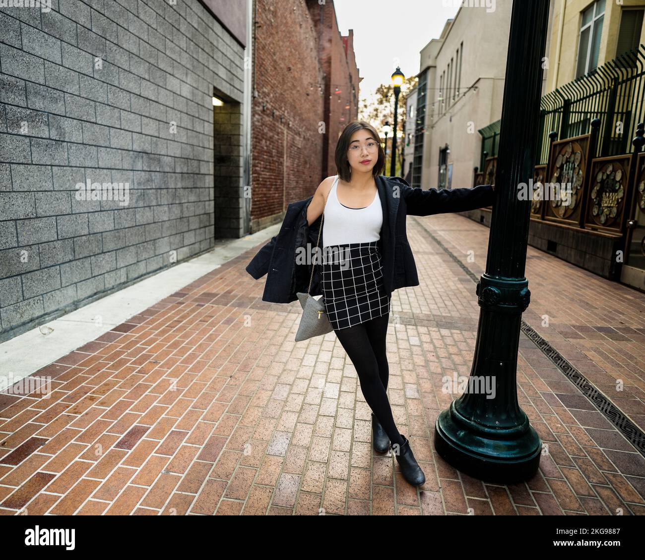 Mujer Joven Joyosa Swinging en un poste de la lámpara | Vestimenta casual del negocio Foto de stock