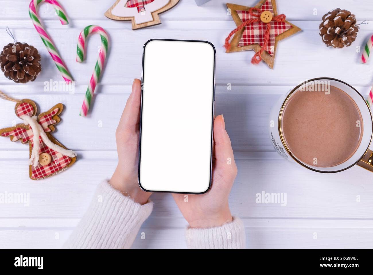 Primer plano mujer sosteniendo el teléfono con pantalla blanca vacía mockup sobre fondo festivo decorado, celebrando la Navidad, el cliente compra en línea, compra Foto de stock