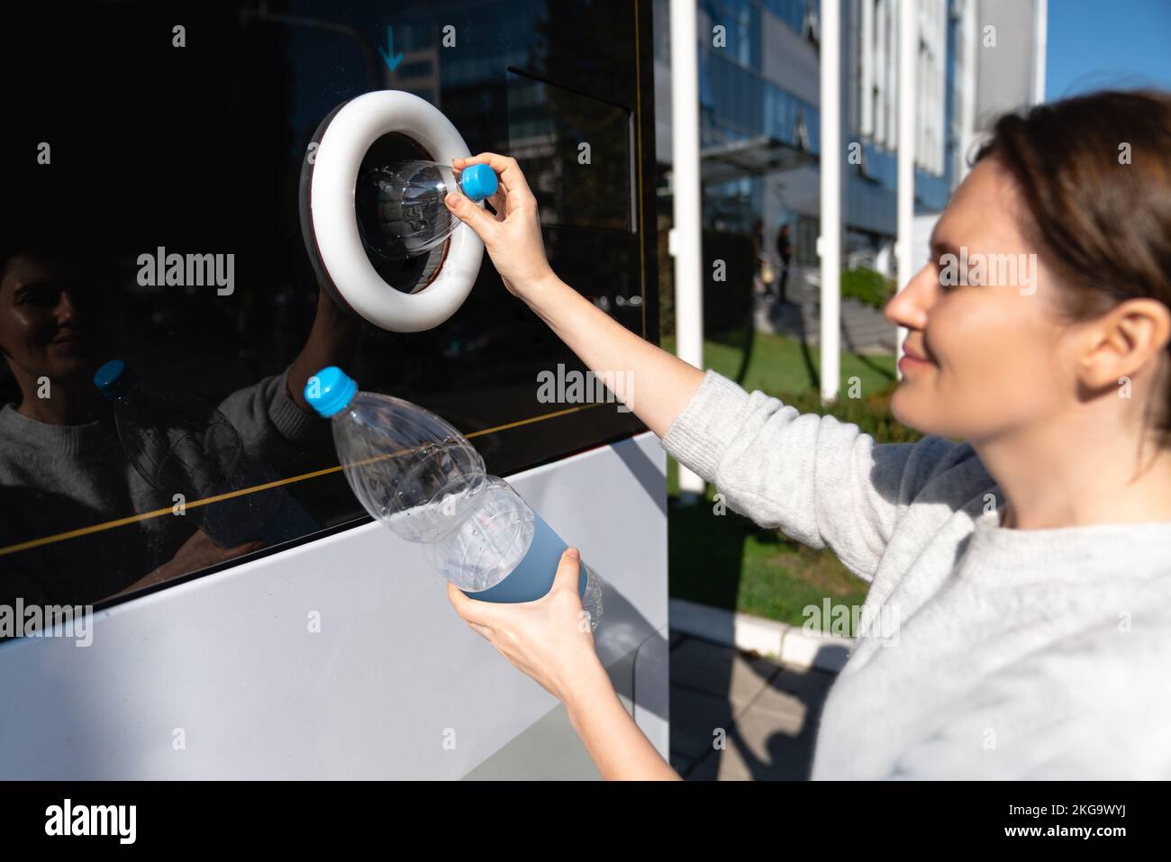 Una mujer utiliza una máquina de autoservicio para recibir botellas y latas de plástico usadas en la calle de una ciudad Foto de stock