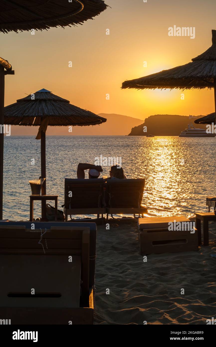 IOS, Grecia - 13 de septiembre de 2022 : Vista de una pareja acostada en las tumbonas, bebiendo vino y disfrutando de la increíble puesta de sol naranja en Ios Grecia Foto de stock
