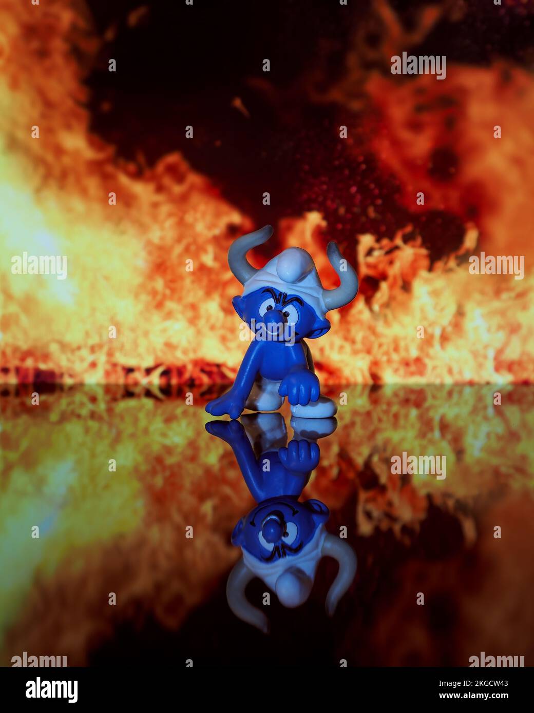 Una fotografía vertical de un pequeño héroe de dibujos animados azul arrodillado con un sombrero con llamas en el fondo Foto de stock