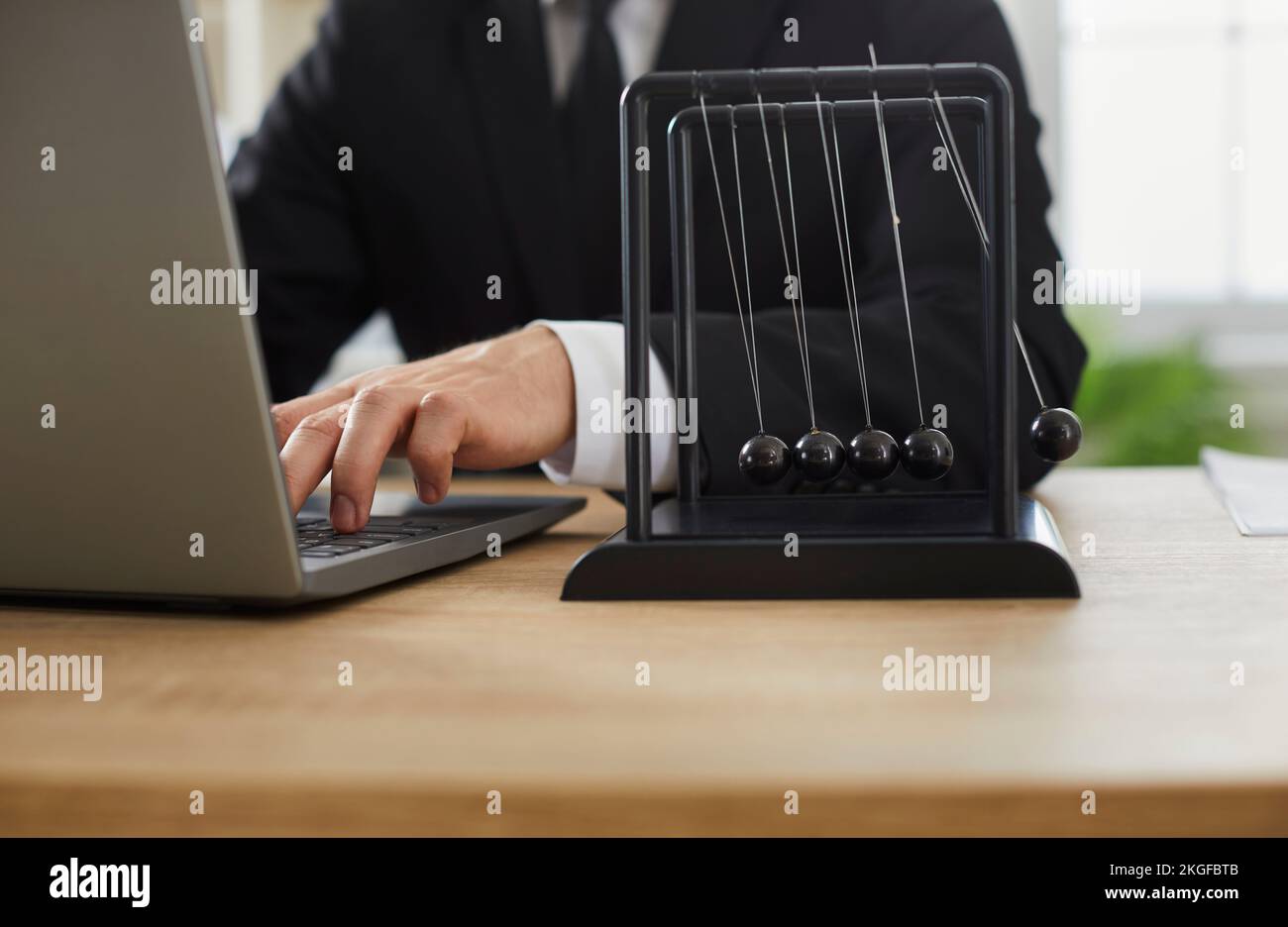 Hombre de negocios que trabaja con un ordenador portátil en el escritorio de su oficina con el péndulo de Newton Foto de stock