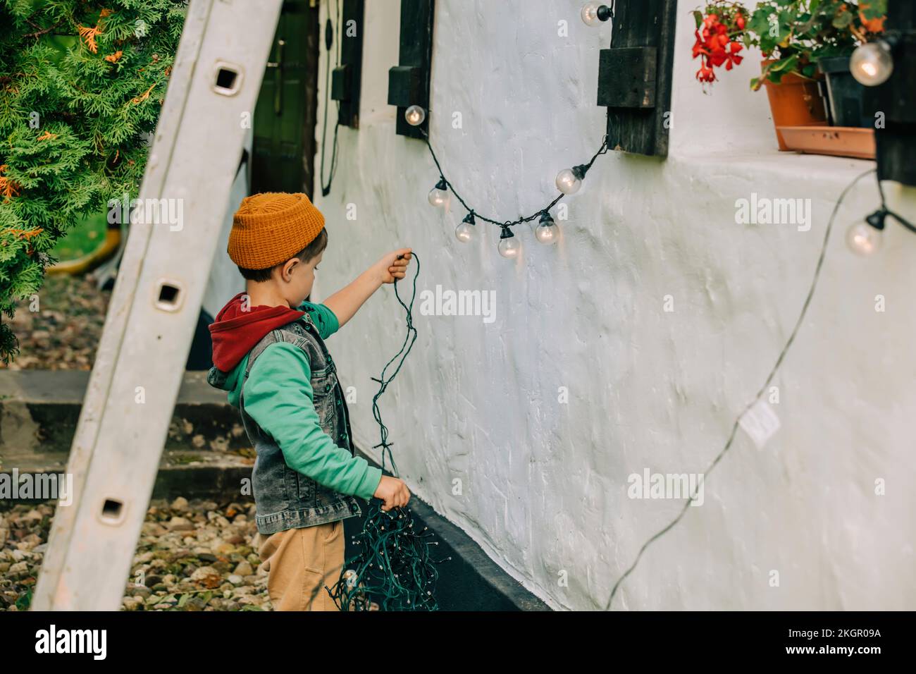 Niño sosteniendo luces de cuerda fuera de la casa Foto de stock