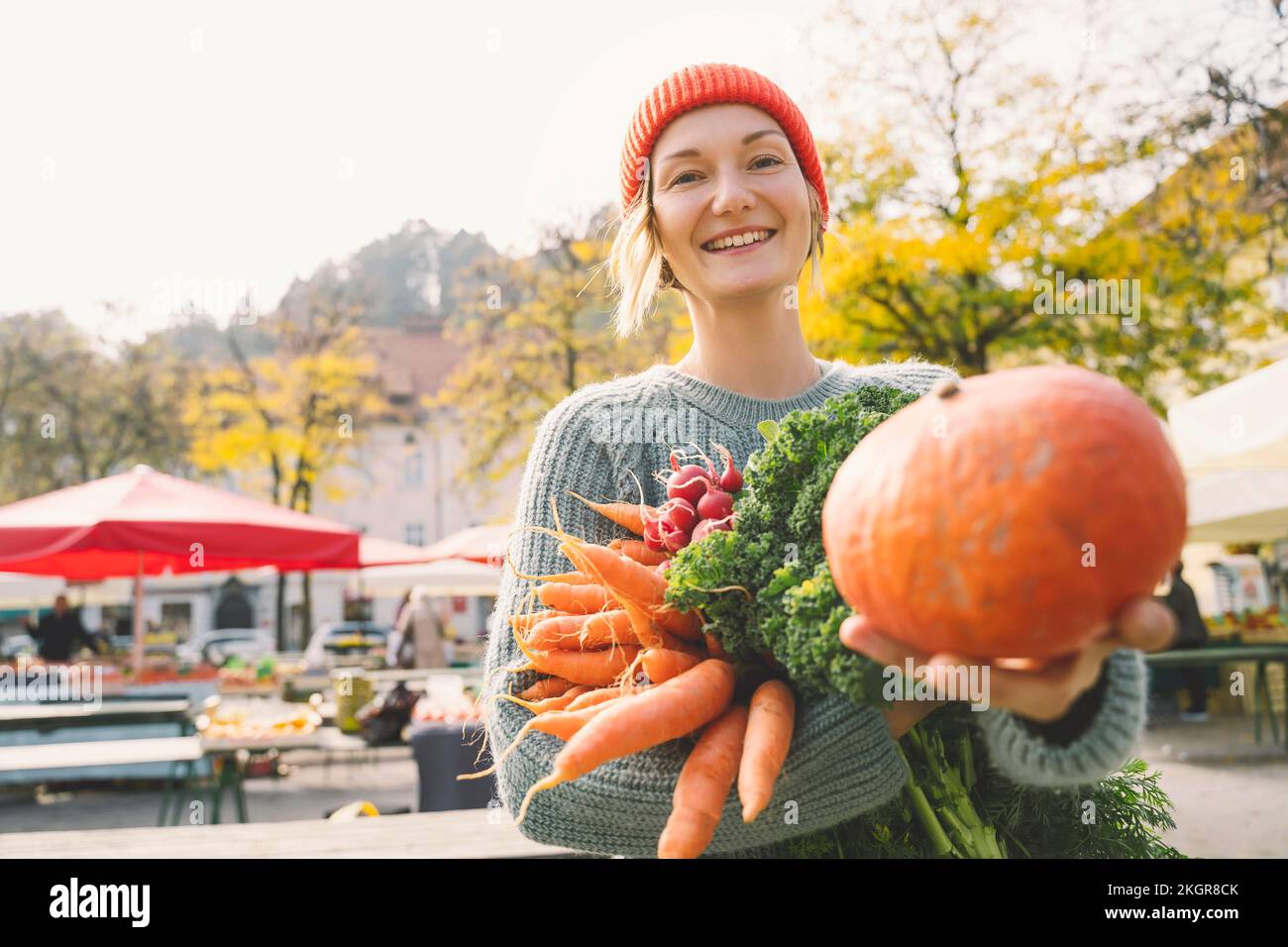 Mujer sonriente sosteniendo verduras frescas mostrando calabaza en el mercado Foto de stock