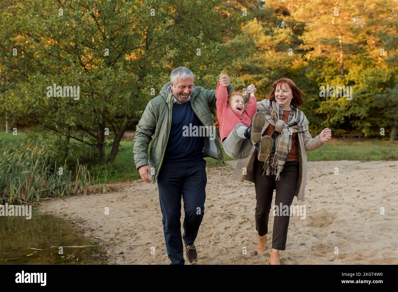 Abuelos divirtiéndose con su nieta caminando sobre la arena Foto de stock