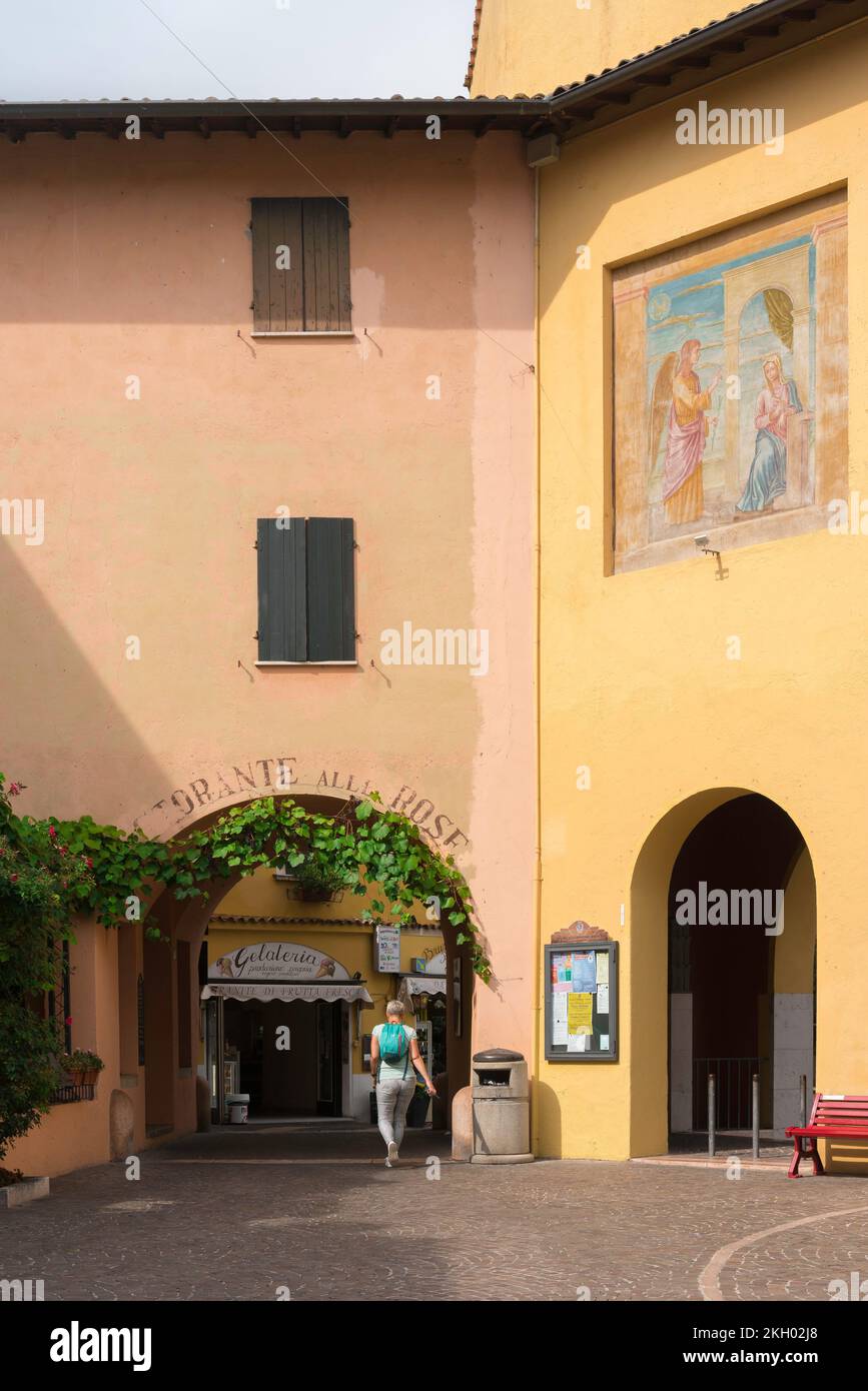 Una mujer viaja sola, vista trasera en verano de una mujer que viaja con una mochila caminando a través de una pequeña plaza pintoresca en un pueblo italiano, Italia Foto de stock