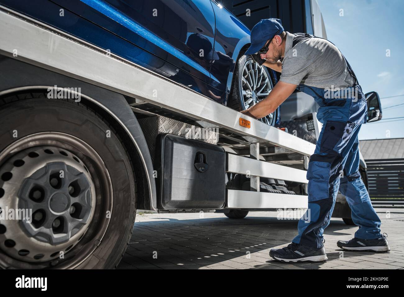 Conductor de camión de remolque Preparándose para entregar de forma segura un vehículo nuevo del concesionario al comprador. Tema de transporte de vehículos. Foto de stock