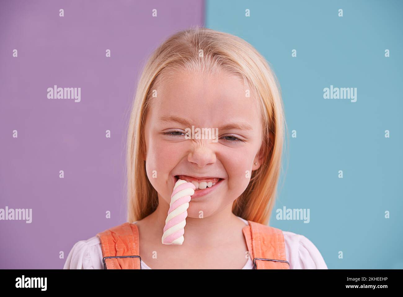 OM nom. Nom. Una pequeña chica linda comiendo dulces contra un colorido fondo. Foto de stock