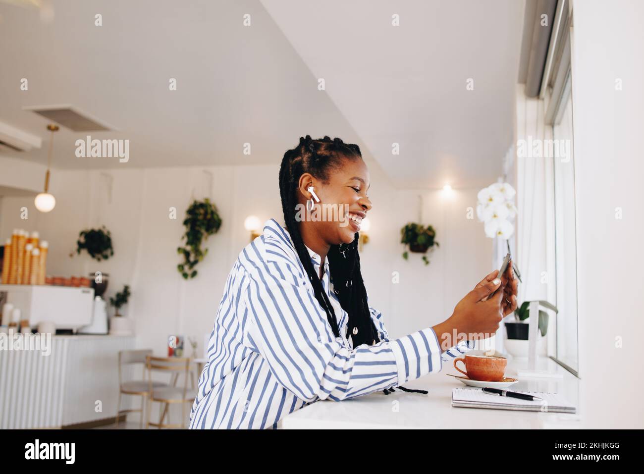Alegre mujer de negocios negra haciendo una videollamada en un smartphone mientras trabaja en una cafetería. Feliz joven empresaria sonriendo mientras que el vídeo chateaba con Foto de stock