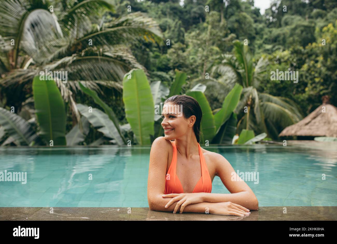 Retrato de una joven feliz que se relaja en la piscina. Mujer de pie en la piscina de un complejo turístico de lujo. Foto de stock