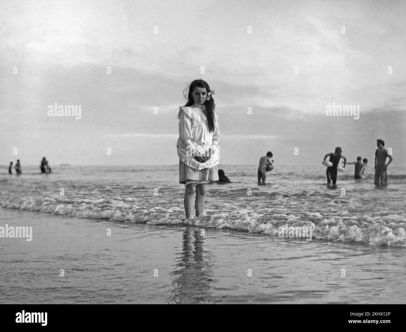 Fotografía en blanco y negro de alate victoriana que muestra a una joven junto al mar, remando al pie desnudo en el borde del agua. Foto de stock