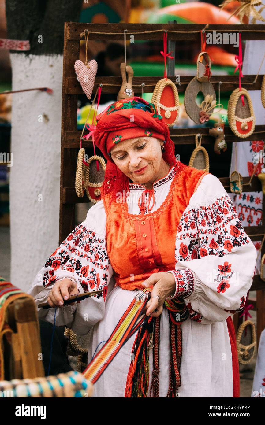 Festival Folk en Minsk, Bielorrusia. Adulto Mujer tejedora en tradicional bordado de ropa bielorrusa muestra el proceso de hilar cinturón. Foto de stock