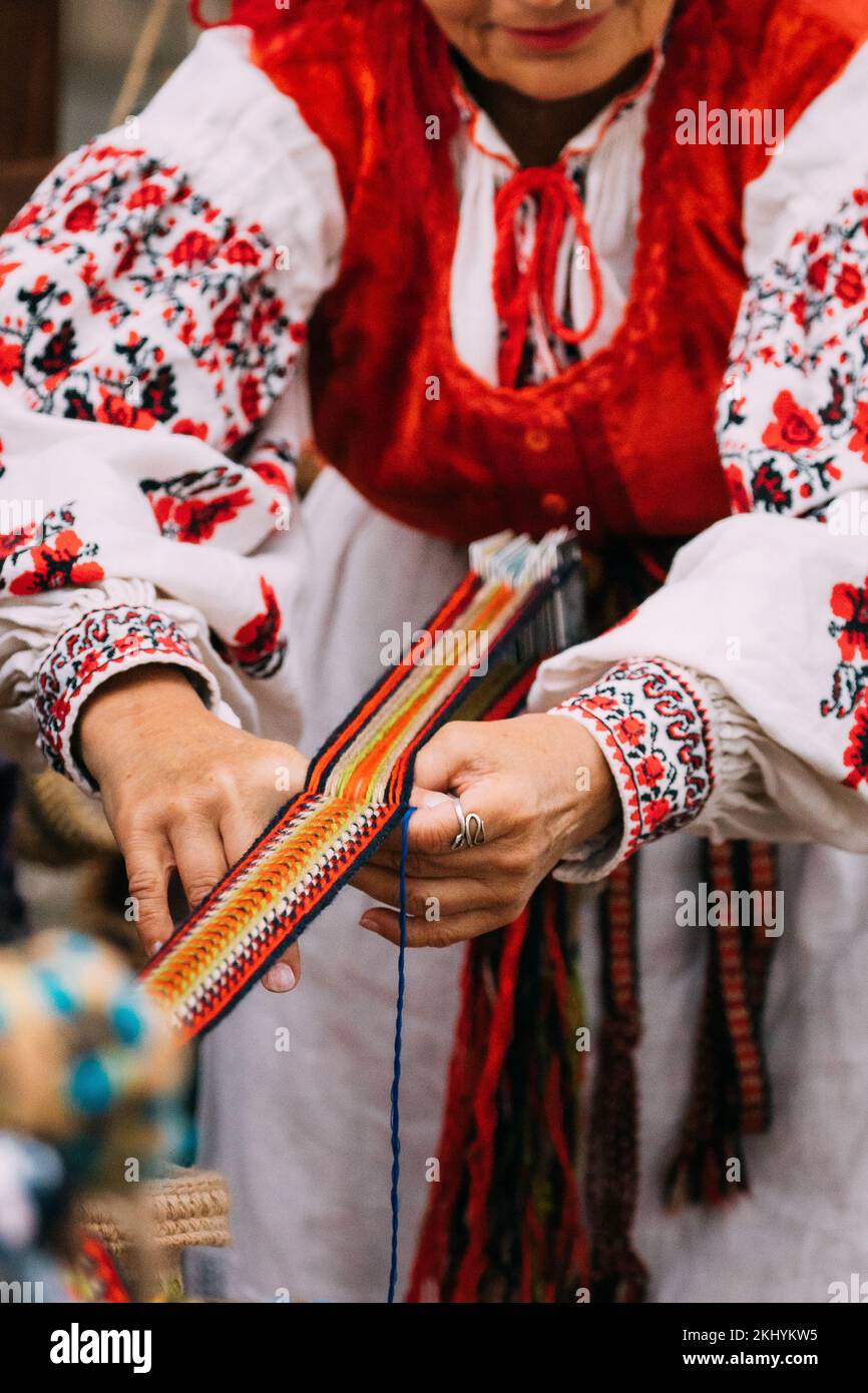 Primer plano de Tejedor Femenino Adulto en la Ropa Tradicional Bordada Bielorrusa muestra el proceso de hilar cinturón. Festival Folk en Minsk, Bielorrusia. Foto de stock
