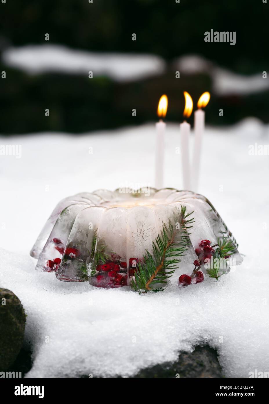 Linterna de Navidad hecha a mano en forma de pastel hecho de hielo, bayas rojas de las caderas, ramas de bayas de acebo y ramas de thuja con velas encendidas en la nieve. Foto de stock