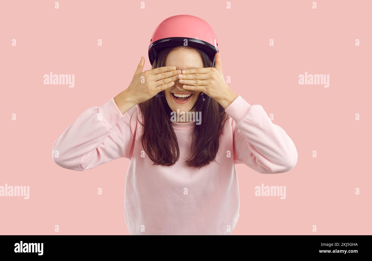 Mujer joven feliz en casco rosa de bicicleta cubre sus ojos en previsión de regalo sorpresa Foto de stock
