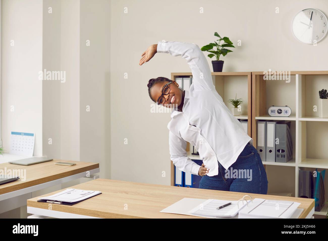 Feliz sonriente joven afroamericana haciendo ejercicios de fitness en el trabajo en la oficina Foto de stock