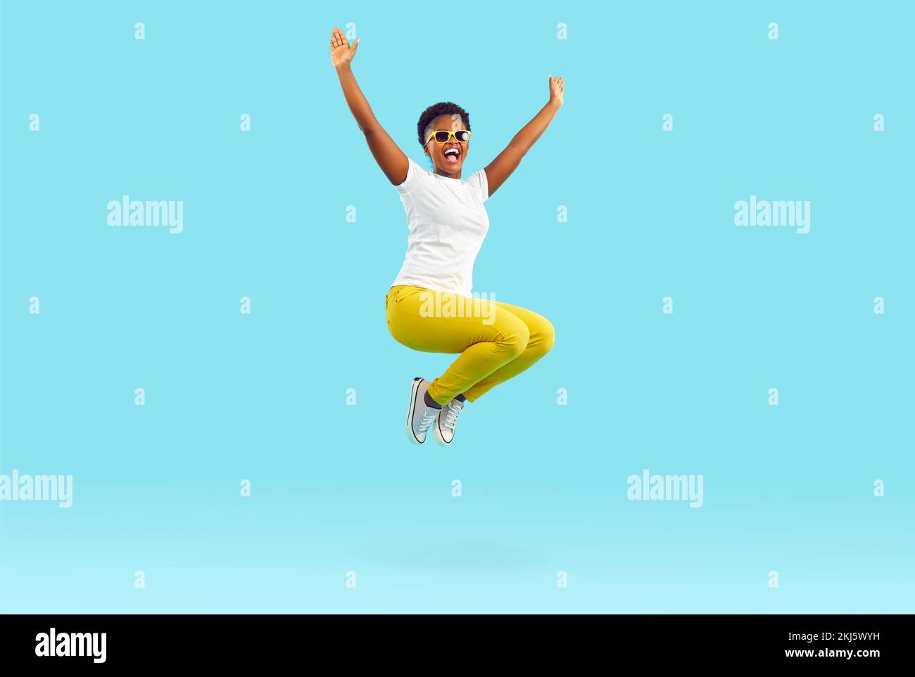 Feliz emocionada joven afroamericana en ropa casual saltando sobre fondo azul Foto de stock