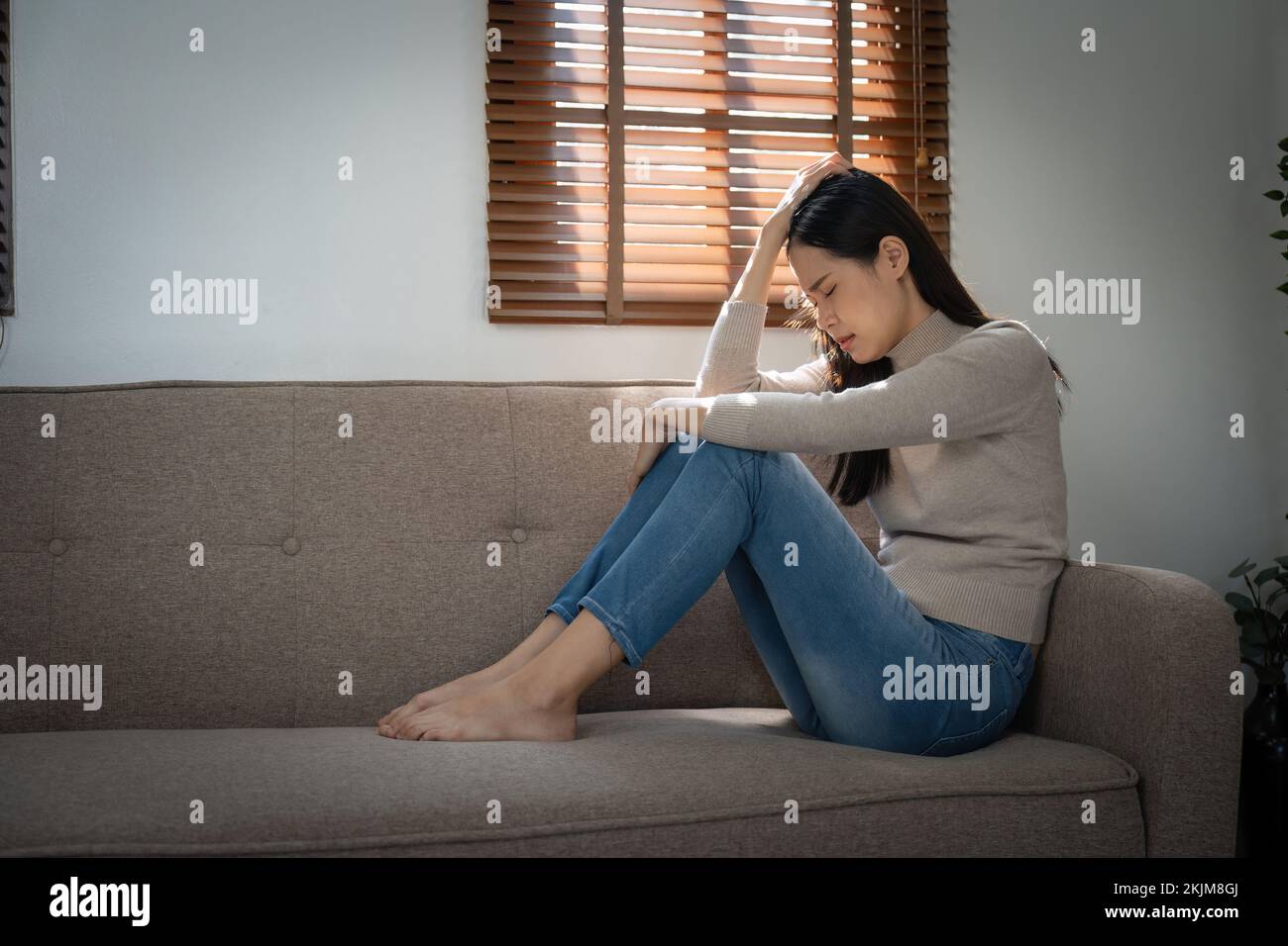 Joven solitaria atractiva mujer asiática llorando en el sofá sentirse triste cansado y preocupado sufriendo depresión aislado en casa. Salud mental y bloqueo Foto de stock