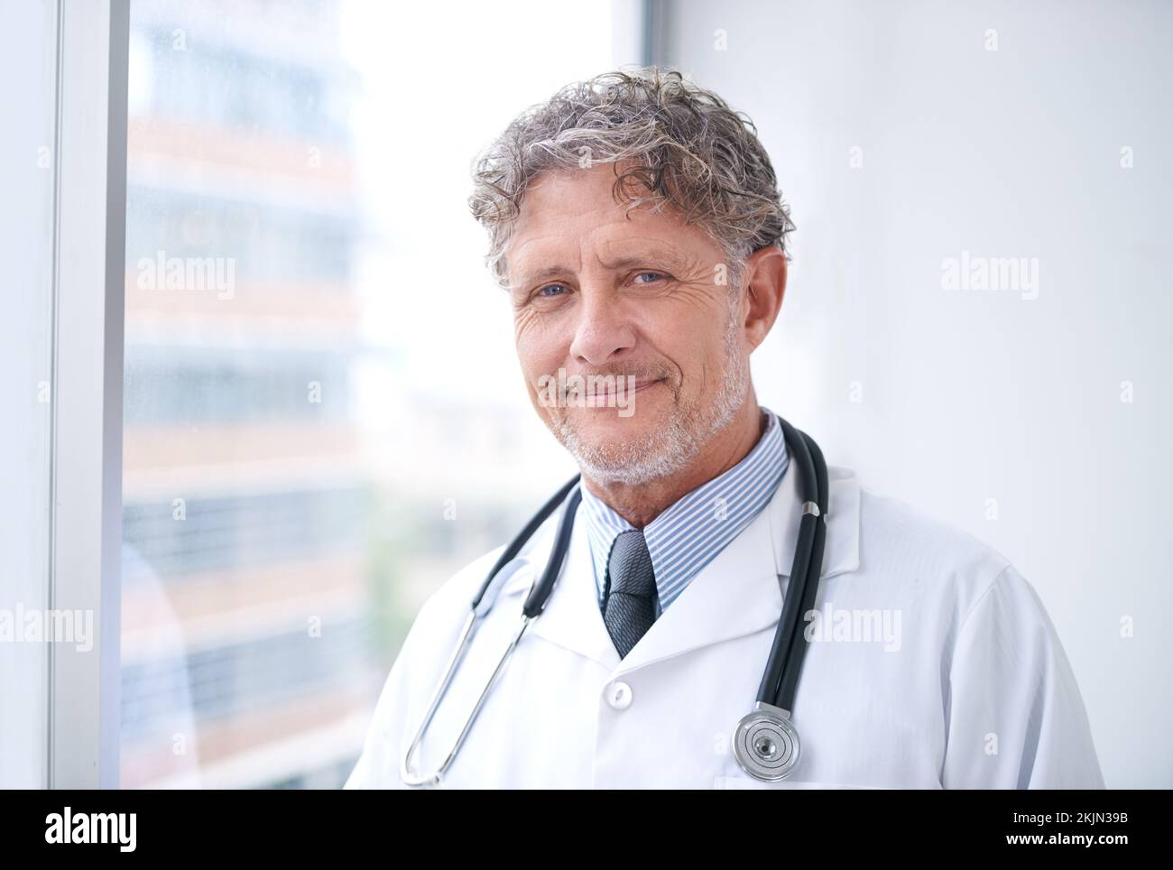 Su cuidado es la máxima prioridad. Retrato de un sonriente médico maduro de pie en su oficina. Foto de stock
