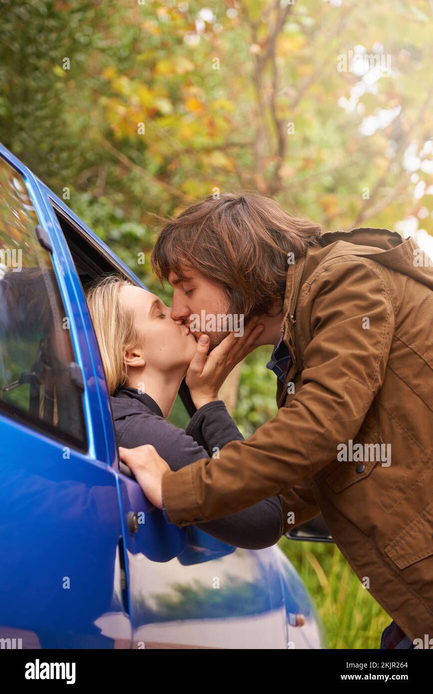 Despedidas persistentes. Una joven pareja besándose entre sí Adiós a través de la ventana de un coche. Foto de stock