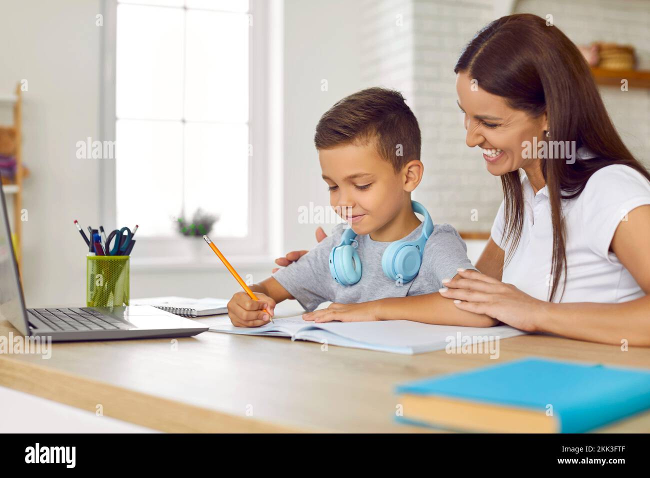 Feliz, sonriente madre ayudando a su hijo pequeño mientras él está haciendo su tarea escolar Foto de stock