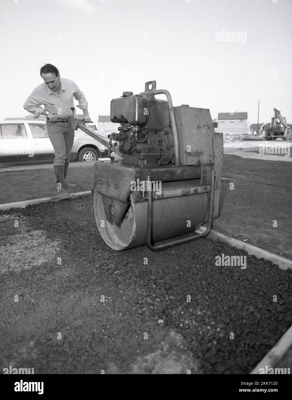 1980s, histórico, un hombre repavimentando un camino de una casa, usando un pequeño rodillo de la carretera de la época, también conocido como compactador, para acostarse en el asfalto, Inglaterra, Reino Unido. Foto de stock