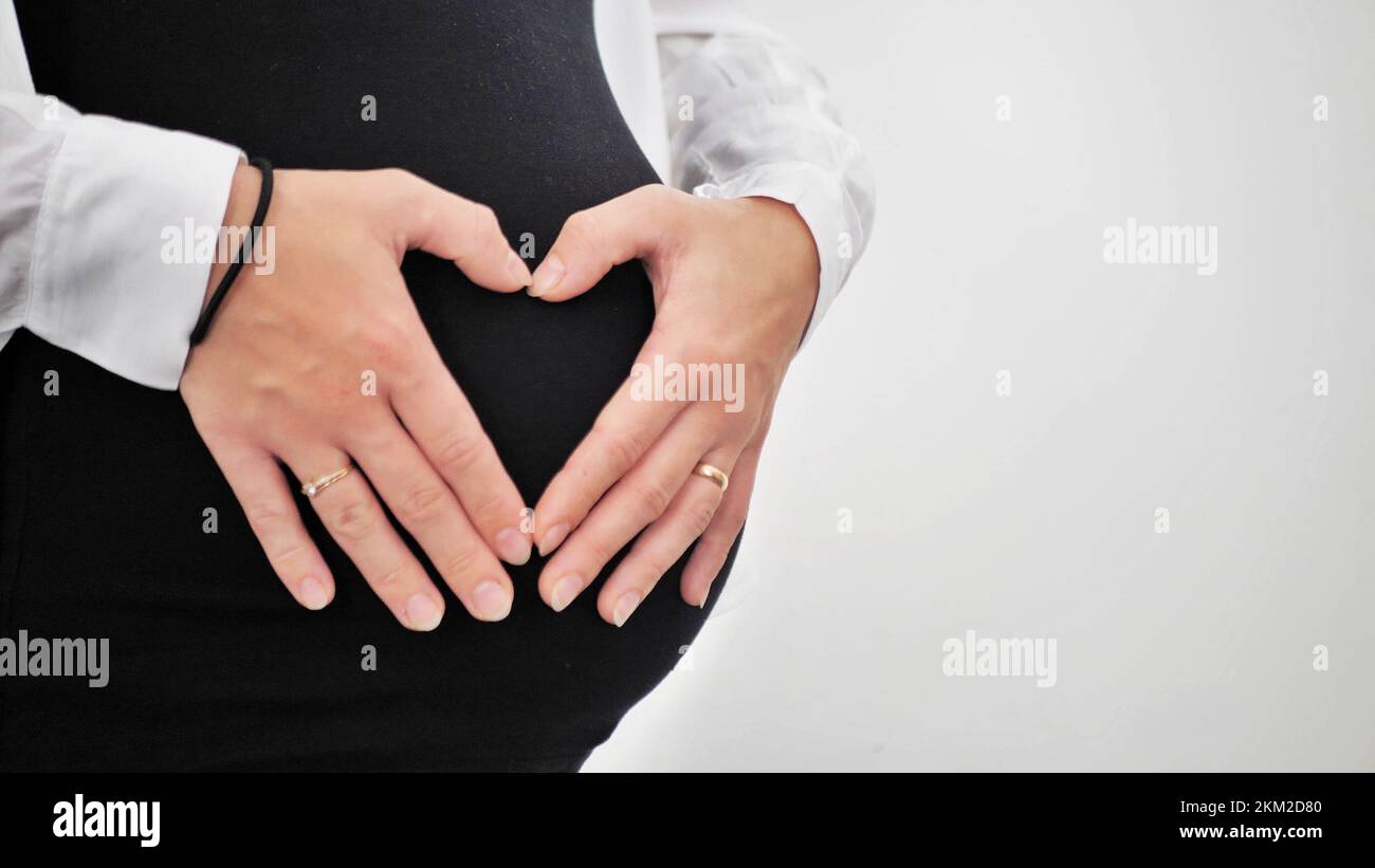 Mujer embarazada sosteniendo sus manos en forma de corazón sobre la  protuberancia de su bebé. Vientre embarazada con dedos símbolo de corazón.  Concepto de maternidad, Ducha de bebé Fotografía de stock -
