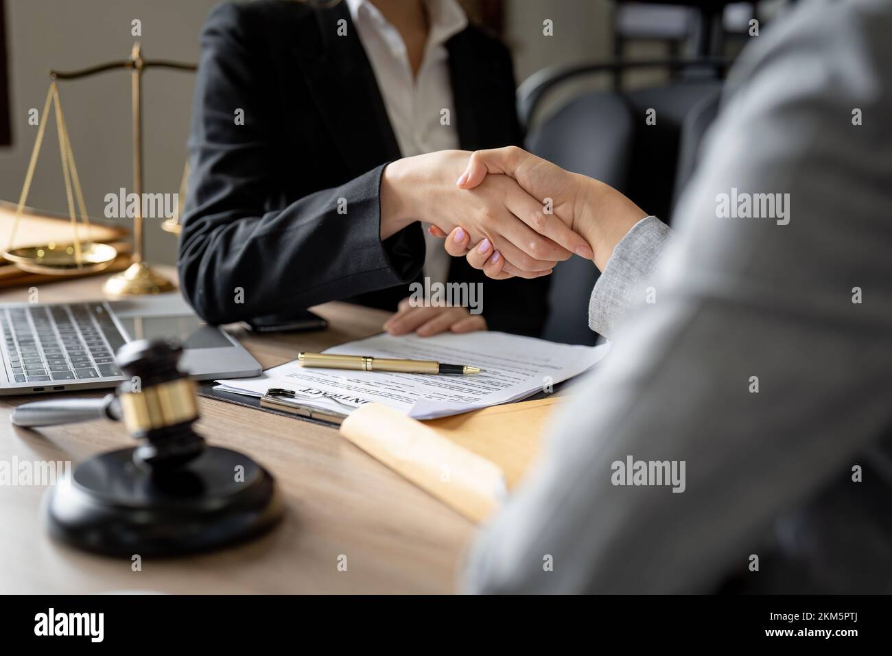 Martillo de justicia sobre mesa de madera con juez y cliente estrechando las manos después de aconsejado en el fondo en la sala de tribunal, concepto de servicio de abogado. Foto de stock