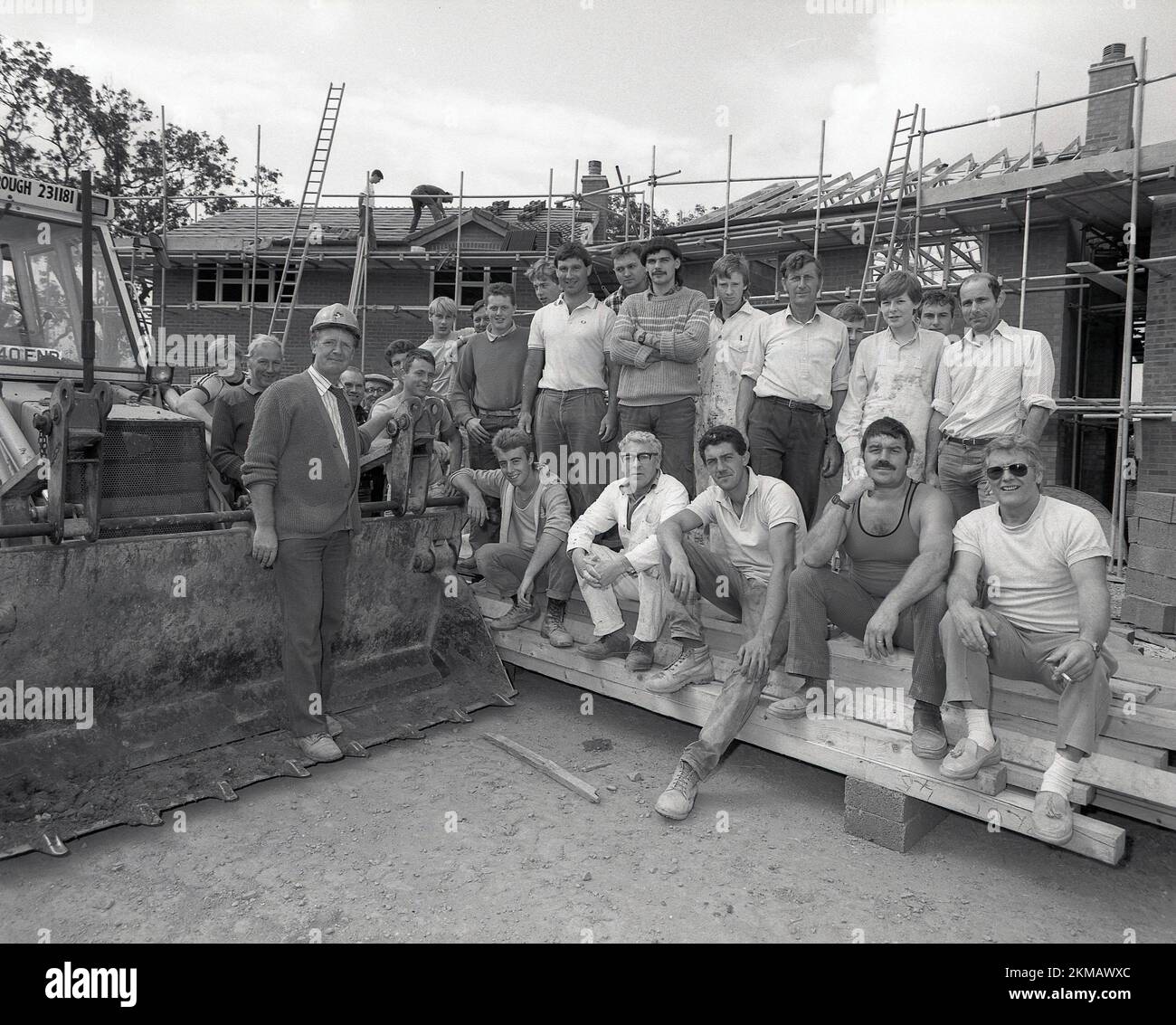 1980s, histórico, fuera en un sitio de construcción de casas nuevas, el equipo de trabajadores se reúne junto a un excavador para una foto de grupo, Inglaterra, Reino Unido. Foto de stock