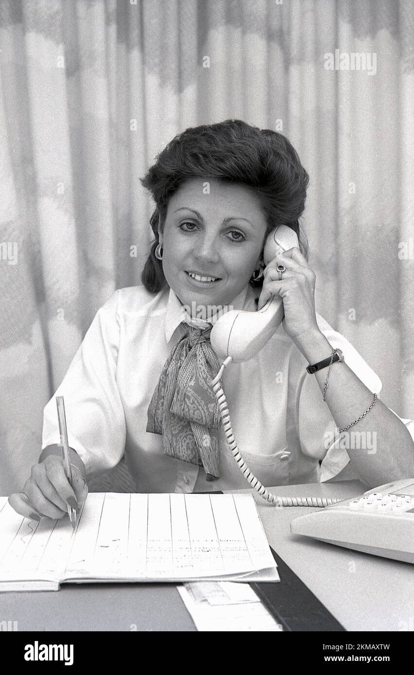 1980s, histórica, una dama de ventas de nuevos hogares que usan una blusa, con cuello y bufanda de seda en un escritorio en el teléfono, con un horario de citas en una libreta de papel, Inglaterra, Reino Unido. Foto de stock
